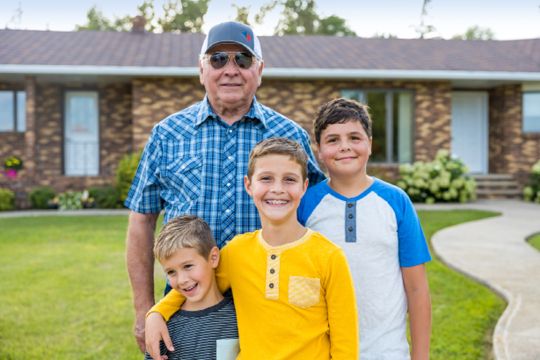 Family posing and smiling in front of house