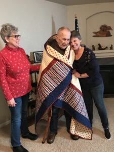 man with quilt hugged by family member